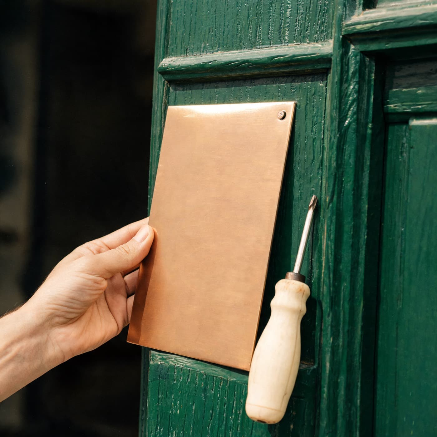 A blank copper plaque being held against a deep green painted door.