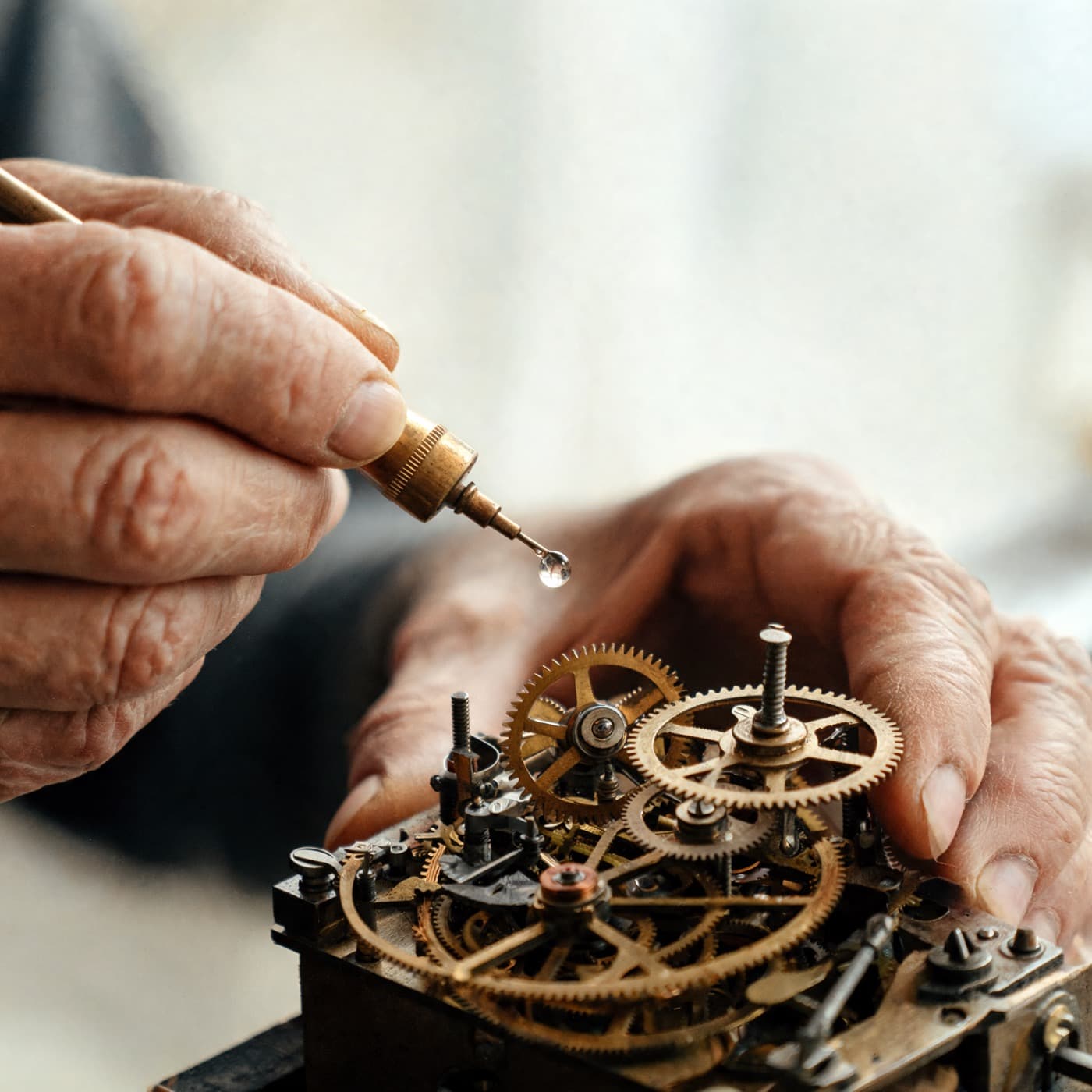Two hands oiling the brass mechanism of an old clock.