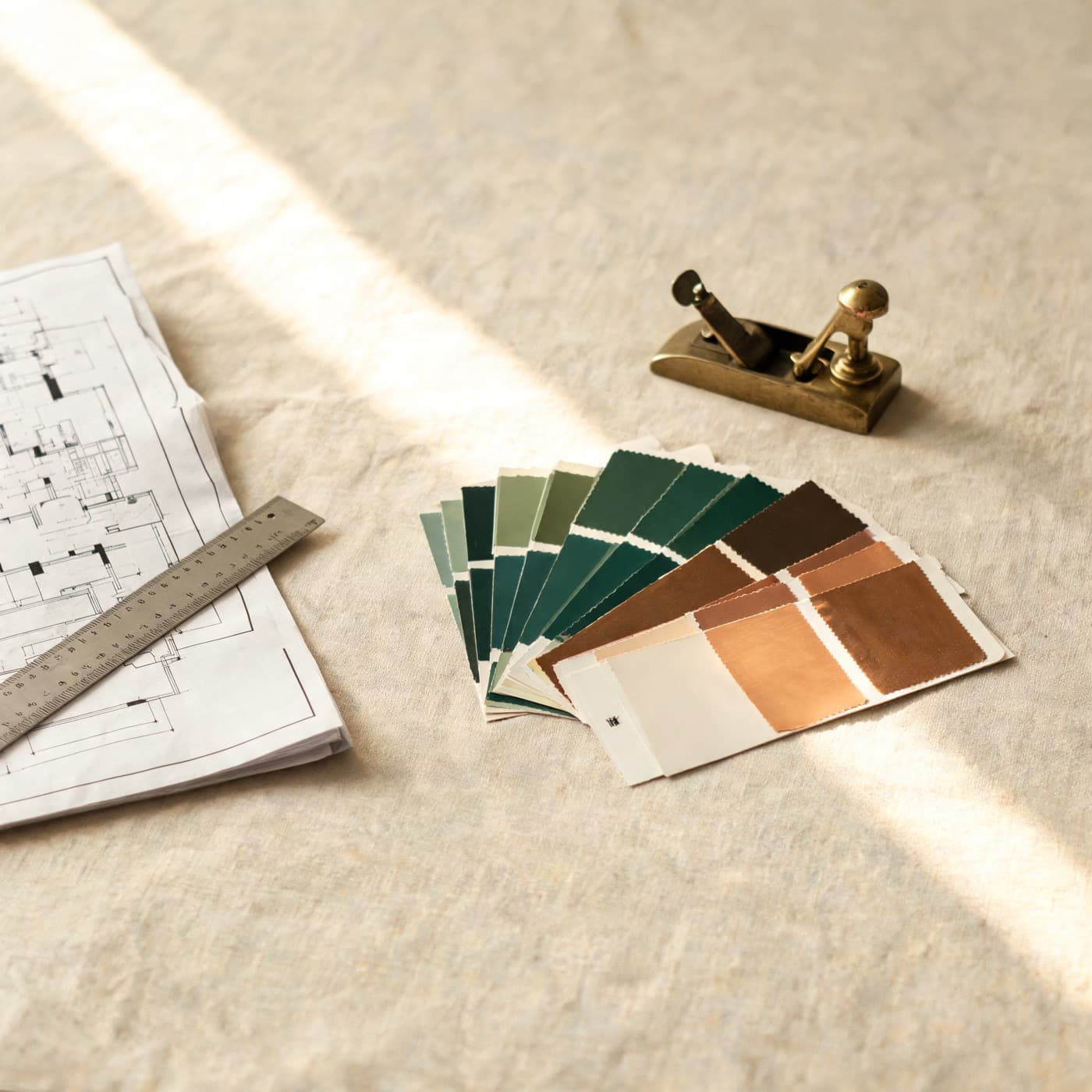 A workbench with a folded drawing, a steel rule, paint chips in green and copper, and a small brass plane.