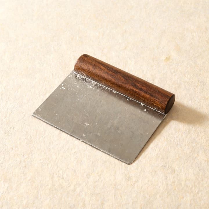 A well-used dough scraper, photographed on bone-coloured paper.